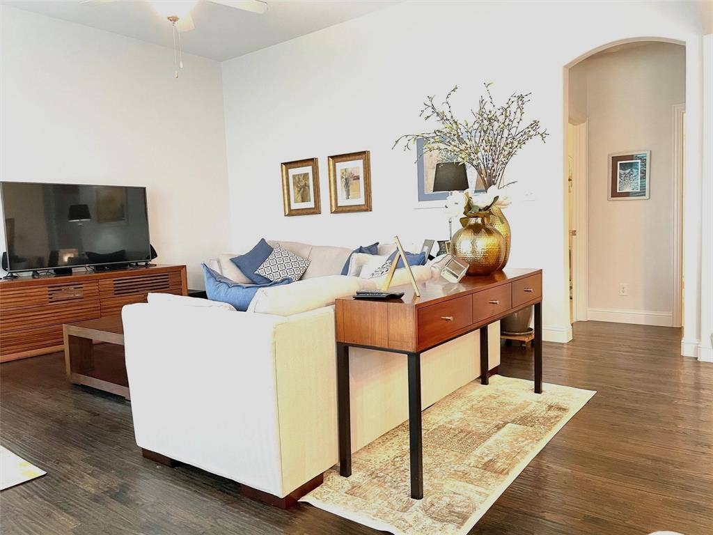 Living area featuring wood-finish flooring, vaulted ceilings, a ceiling fan with integrated light fixture, and an arched doorway
