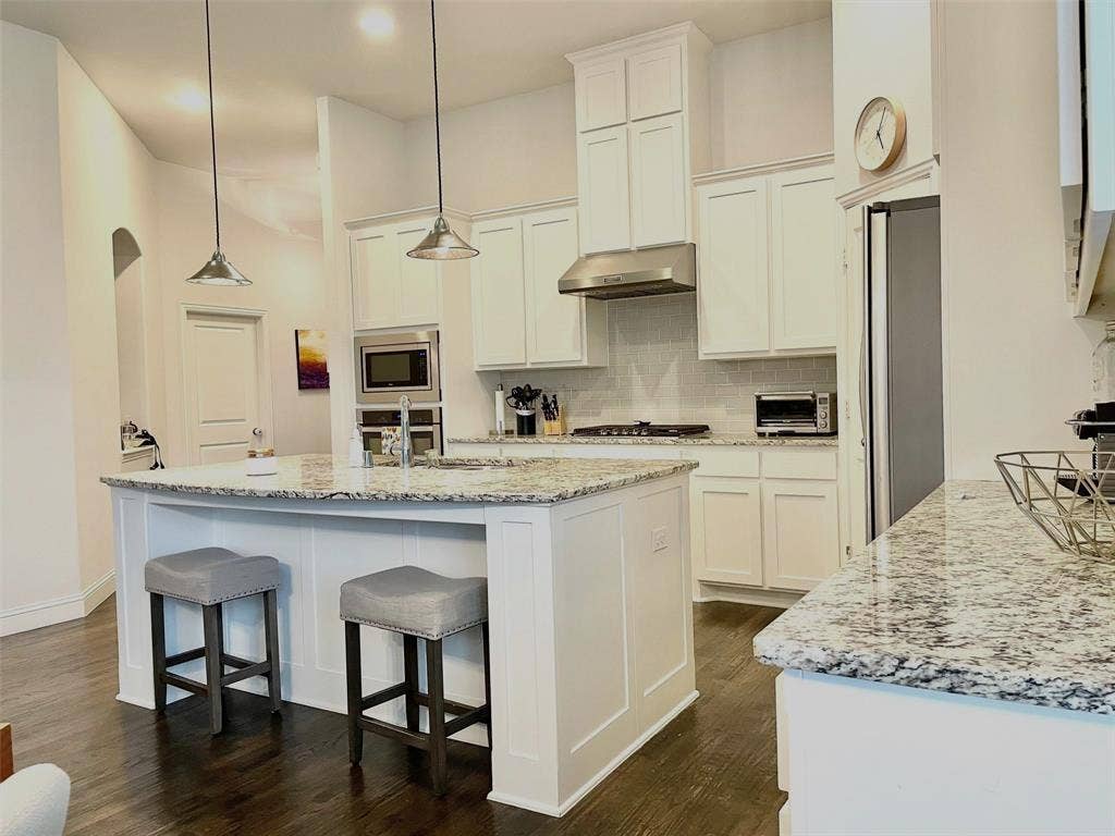 Kitchen featuring white cabinetry, stone countertops, a center island with pendant lighting, stainless steel appliances, and wood-finish flooring