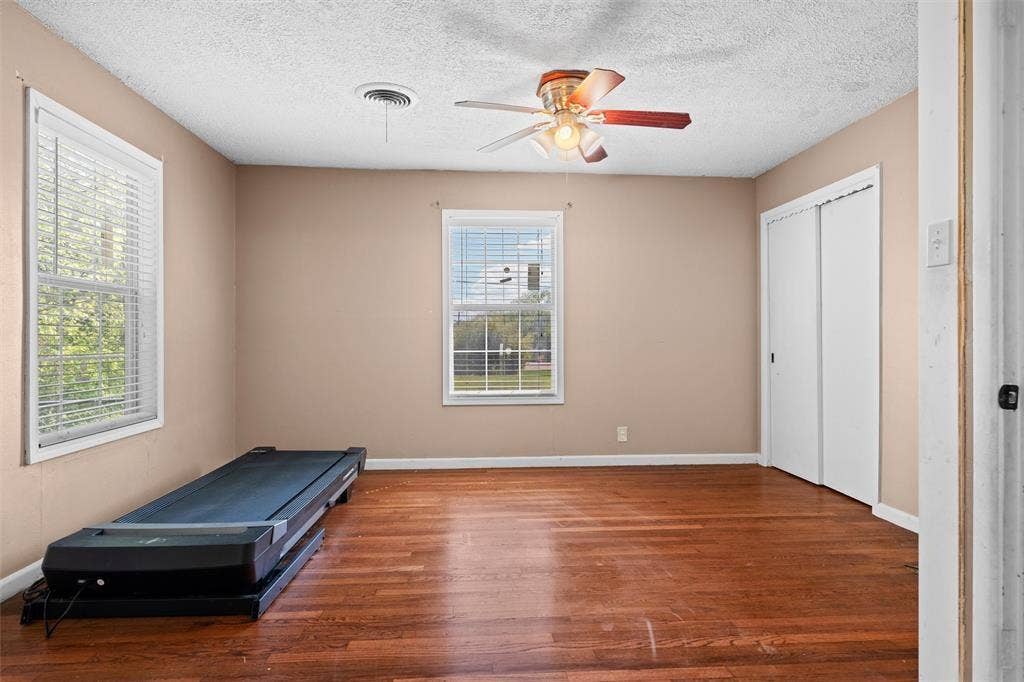 3401 E University Drive, McKinney, TX 75069 Room featuring wood-finish flooring, two windows with horizontal blinds, a ceiling fan with integrated lighting, and a closet with sliding doors