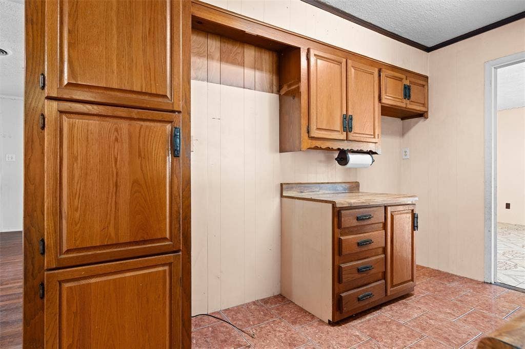 3401 E University Drive, McKinney, TX 75069 Kitchen area featuring wood cabinetry, laminate countertops, tile flooring, and integrated wall-mounted storage