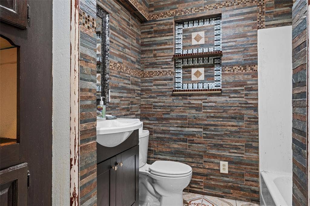3401 E University Drive, McKinney, TX 75069 Bathroom featuring full-height stacked stone wall cladding, built-in tiled recessed shelving, dark wood-finish cabinetry, and ceramic tile flooring