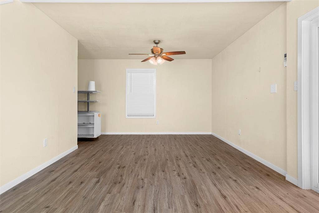 3401 E University Drive, McKinney, TX 75069 Neutral-toned room featuring wood-finish flooring, a single window with blinds, and a ceiling-mounted fan with integrated lighting
