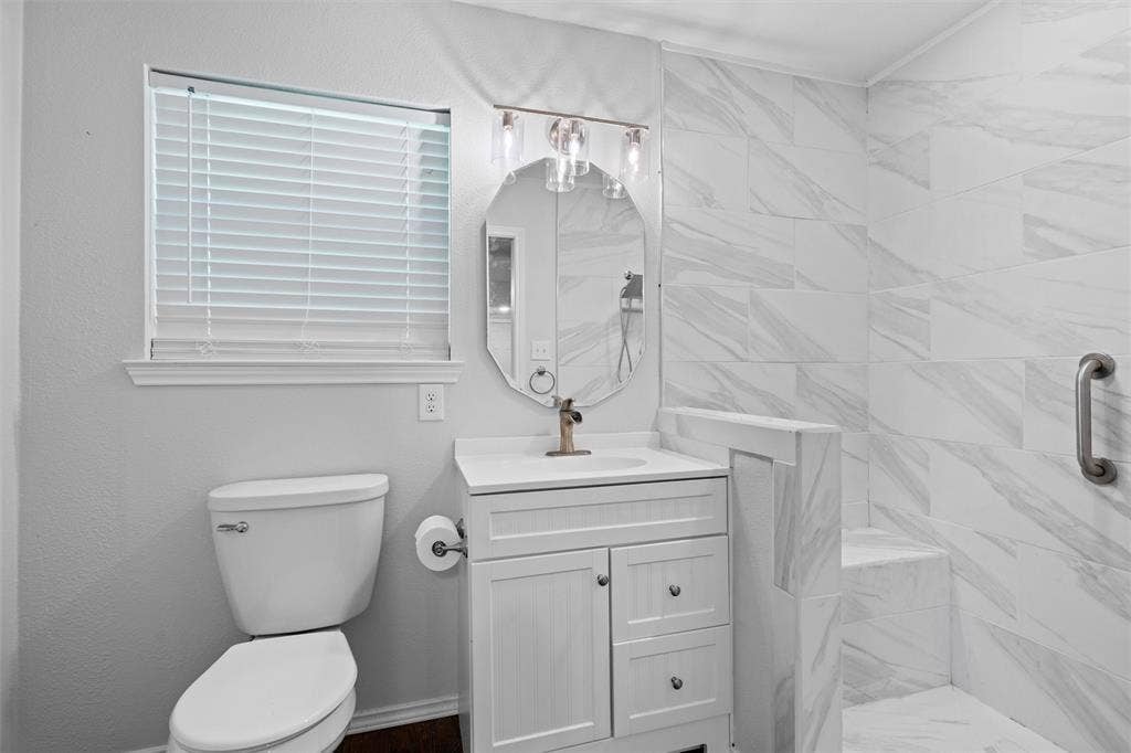 3401 E University Drive, McKinney, TX 75069 Bathroom featuring a white vanity cabinet with an integrated countertop, oval wall-mounted mirror, three-light fixture, and a tiled shower stall with a built-in bench
