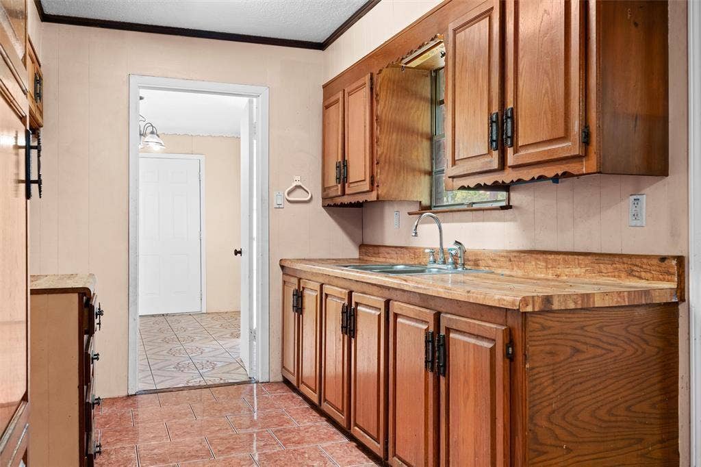 3401 E University Drive, McKinney, TX 75069 Kitchen featuring wood cabinetry, integrated wood-finish countertops, stainless steel sink with metal fixtures, and ceramic tile flooring