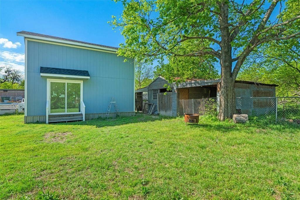 3401 E University Drive, McKinney, TX 75069 Two-story structure with board and batten siding, sliding glass doors, metal roof, detached secondary structure, and mature trees