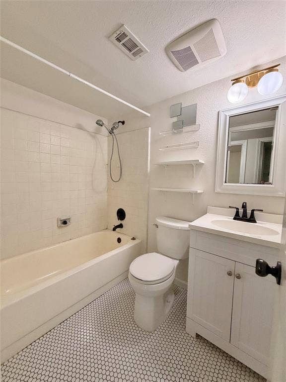 Bathroom featuring a white vanity cabinet with a stone-top integrated sink, black dual-handle faucet, white tile shower surround with a handheld shower head, and small-format hexagonal floor tiling
