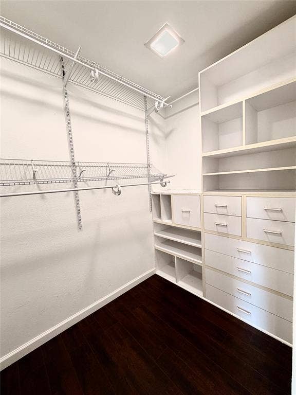 Walk-in closet featuring white built-in cabinetry, multiple drawers, open shelving, integrated wire racking, and dark wood-finish flooring