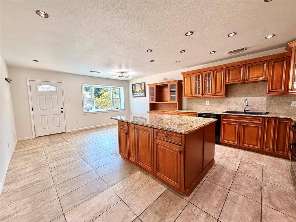 Kitchen featuring wooden cabinetry, a central island with a stone-finish countertop, tiled flooring, recessed lighting, and a neutral-toned tile backsplash