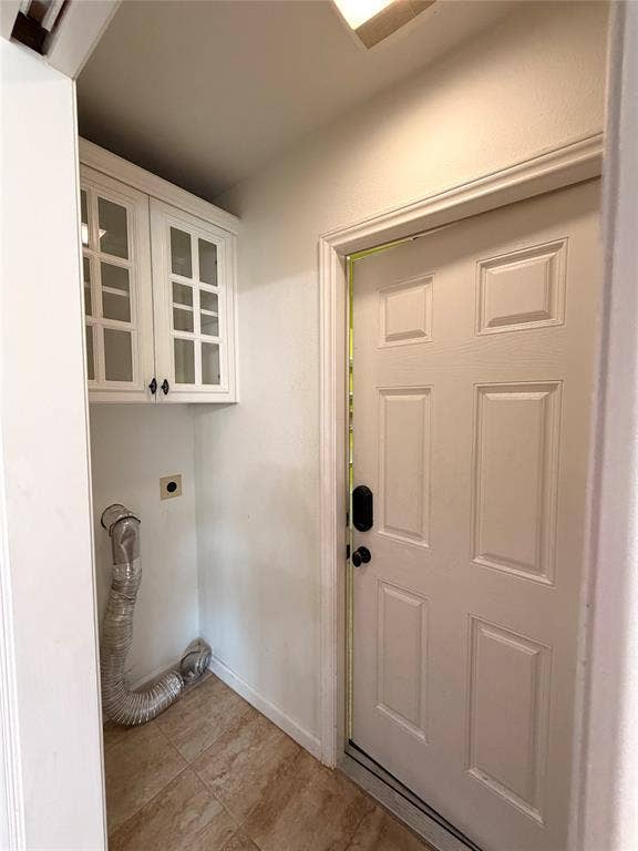 Utility area featuring wall-mounted cabinetry with glass-paneled doors, tiled flooring, and a six-panel door with integrated hardware
