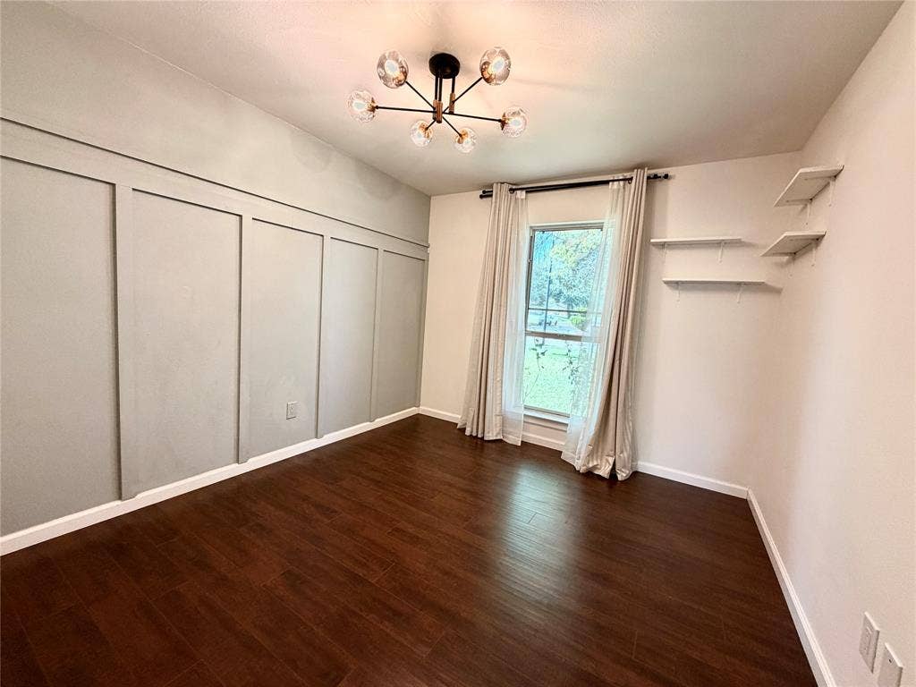 Room featuring wood-finish flooring, a matte black multi-arm chandelier, wall paneling, built-in wall shelving, and a single-pane window