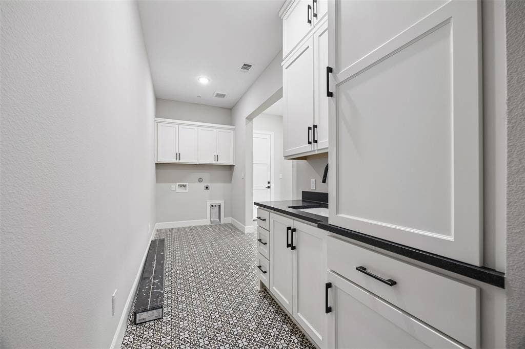 White cabinetry featuring matte black hardware, stone-finish countertops, patterned tile flooring, and integrated wall-mounted cabinetry