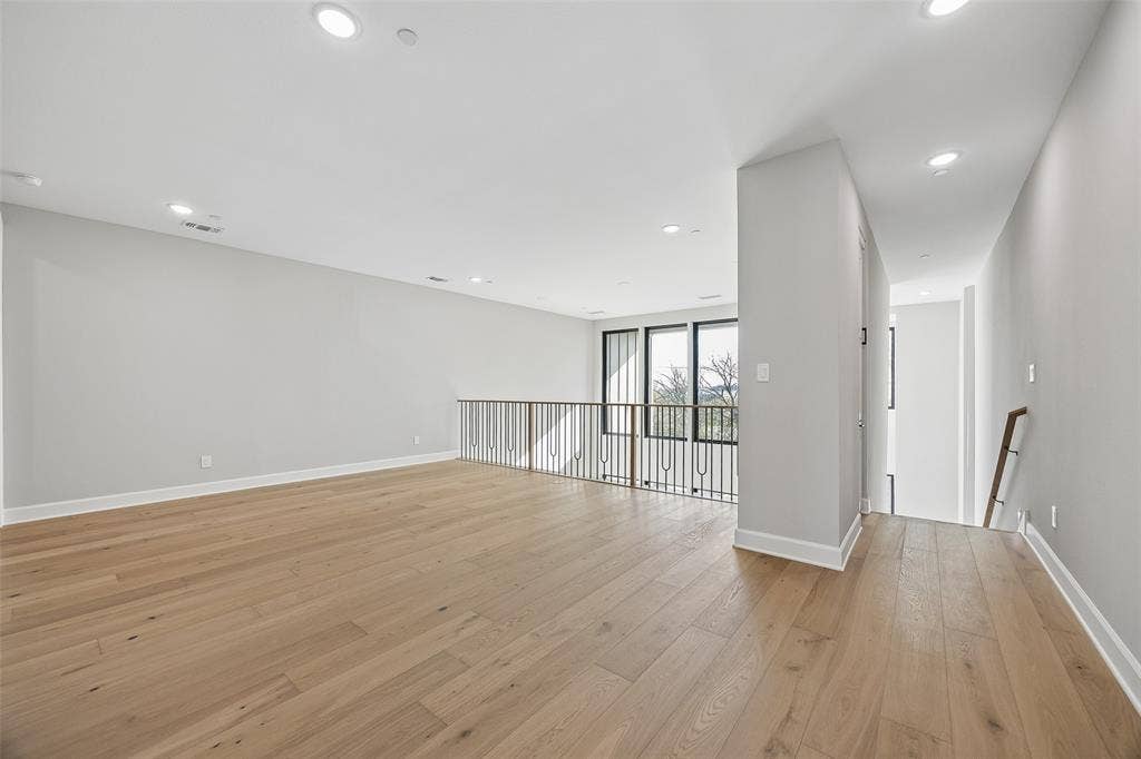 Open-concept space featuring wood-finish flooring, recessed lighting, and a metal railing