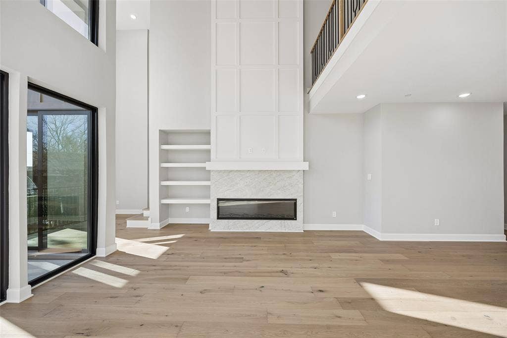 Double-height ceiling featuring wood-finish flooring, a floor-to-ceiling fireplace with stone surround, custom built-in shelving, and metal staircase railing