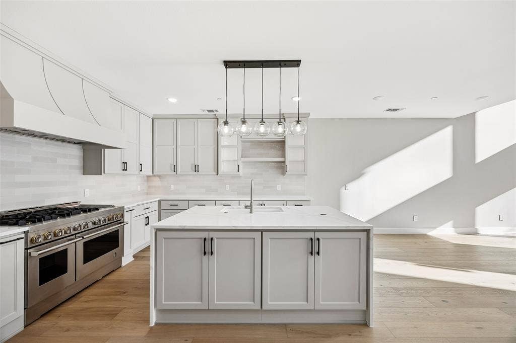 Kitchen featuring light-toned cabinetry, an expansive center island with countertop seating space, a professional-grade stainless steel range with a custom hood, linear tile backsplash, and wood-finish flooring
