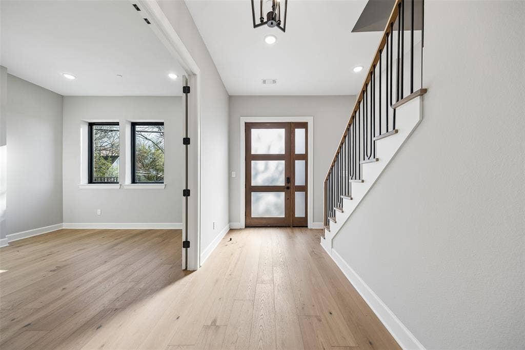 Foyer featuring wood-finish flooring, a multi-panel wood door with glass inserts, and a staircase with matte black metal balusters and a wood handrail