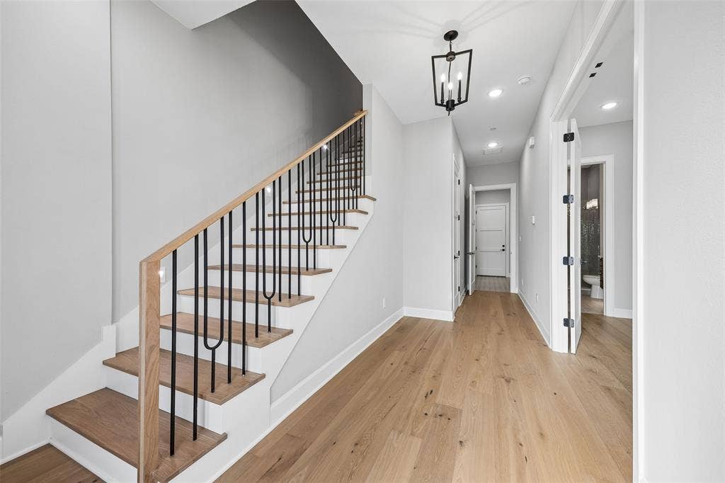 Staircase featuring wood-finish treads and black metal balusters with a wood handrail, light wood-finish flooring, and a contemporary geometric pendant light fixture