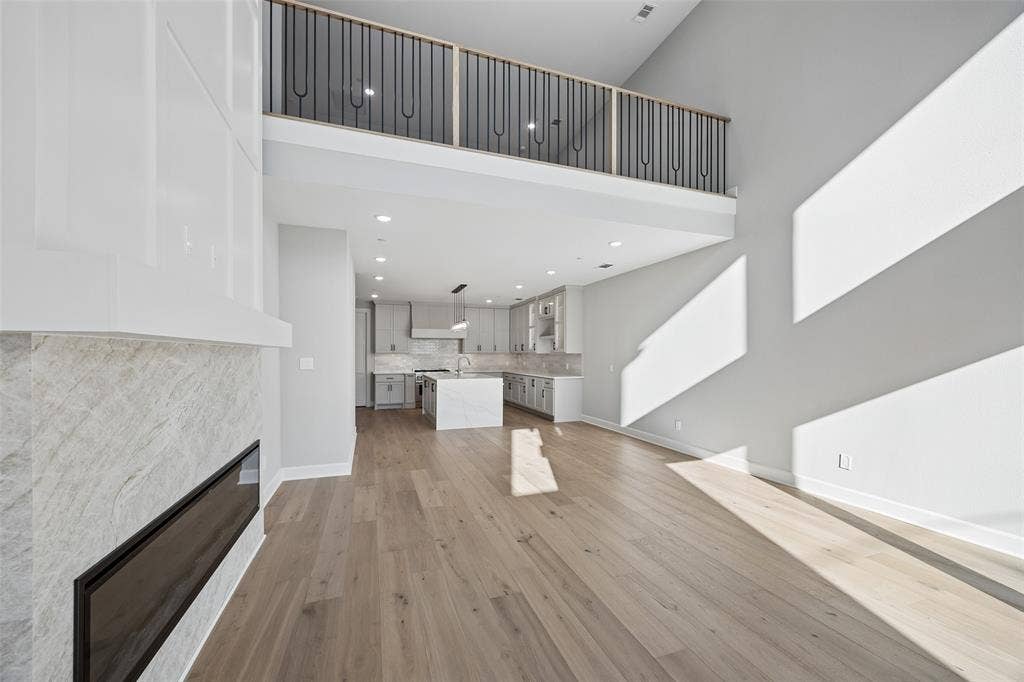 Vaulted ceiling, wood-finish flooring, linear fireplace with stone-finish surround, custom cabinetry, and metal railing