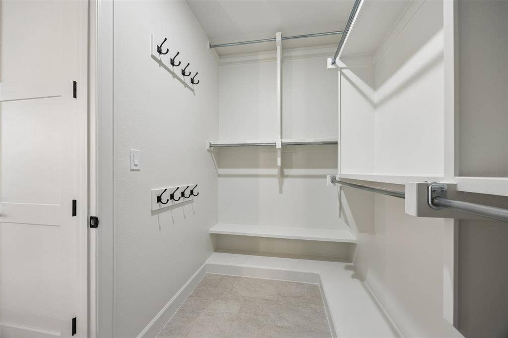 Walk-in closet featuring white built-in shelving, dual-tier metal hanging rods, tiered fixed wall hooks, and light-toned tile flooring