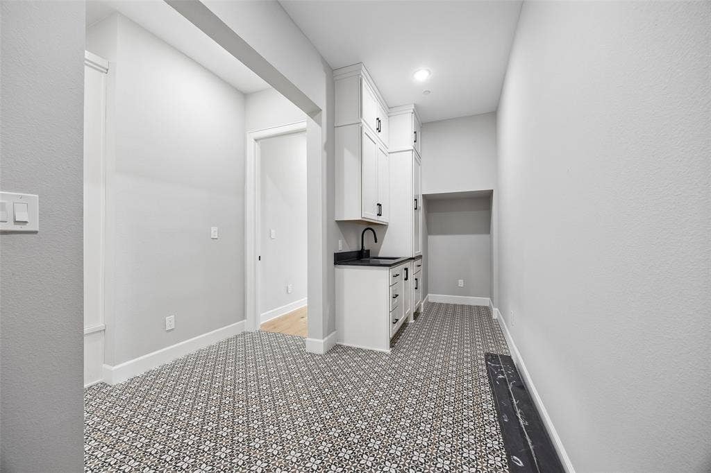 Utility area featuring patterned tile flooring, custom white cabinetry, dark stone countertops, an integrated sink with a matte black faucet, and recessed lighting