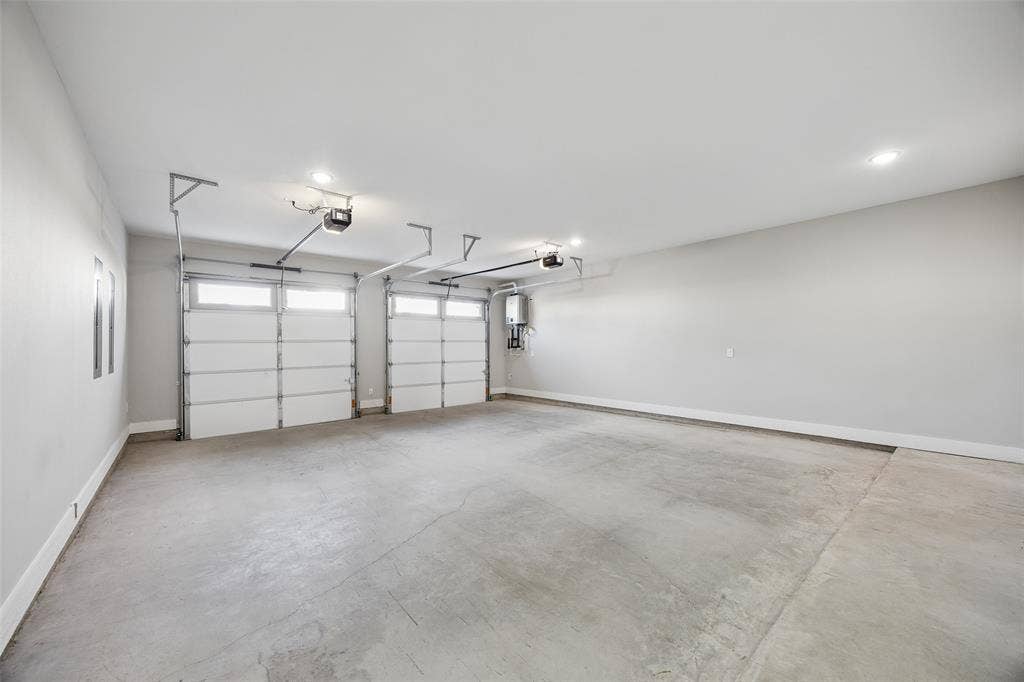 Multi-car garage featuring recessed lighting, two white paneled overhead doors with transom windows, and a wall-mounted tankless water heater