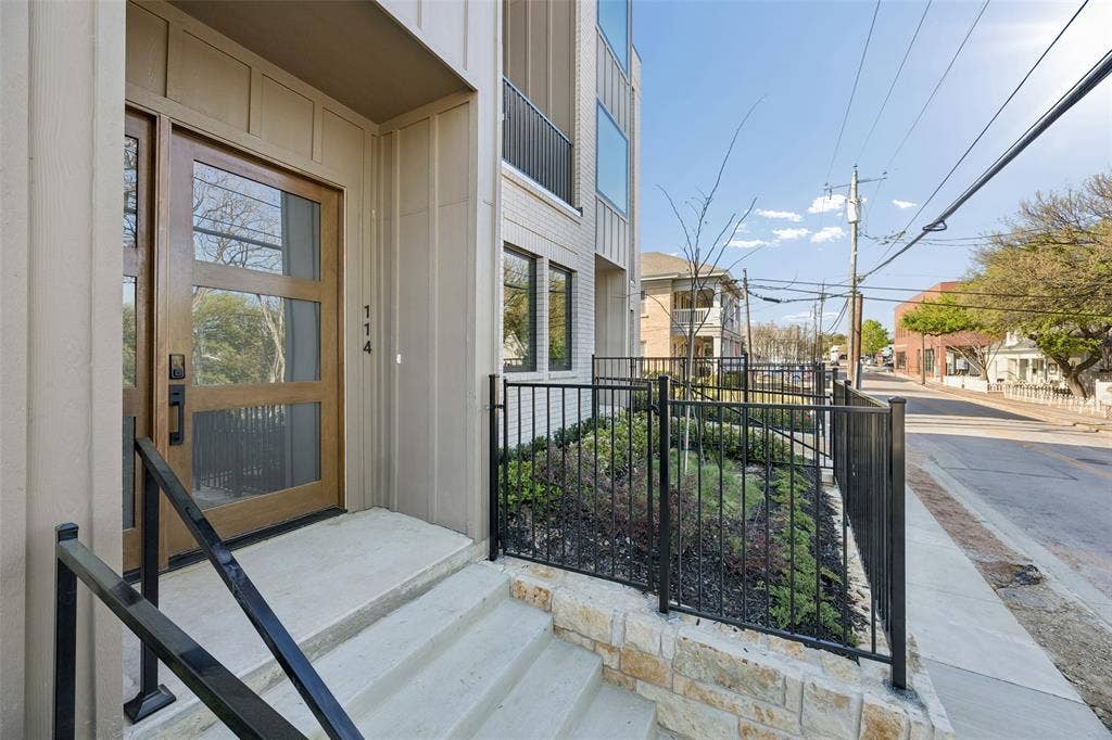 Modern entrance featuring a wood-panel door with glass inserts, concrete steps with black metal handrails, a stone-veneer retaining wall, and black metal fencing