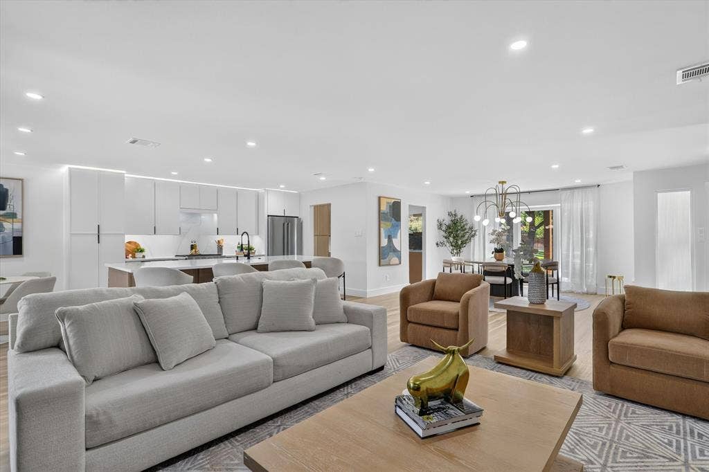 Open-concept interior featuring recessed lighting, a kitchen with flat-panel cabinetry and a waterfall-edge island, wood-finish flooring, and a multi-arm modern chandelier