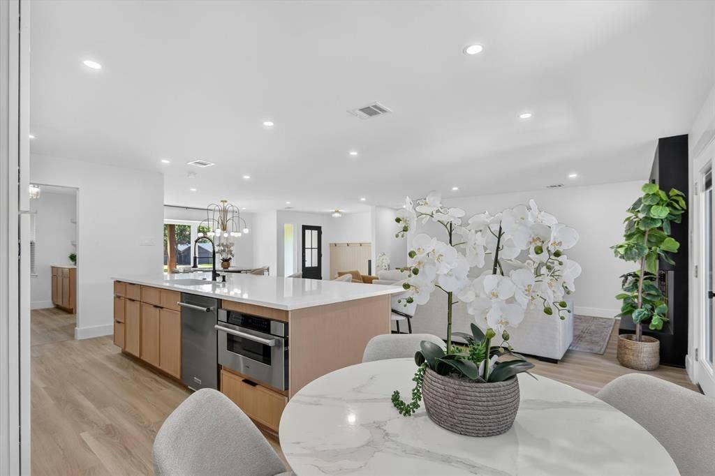 Kitchen featuring a central island with quartz countertops, integrated stainless steel appliances, light-toned cabinetry, and wood-finish flooring with recessed ceiling lighting