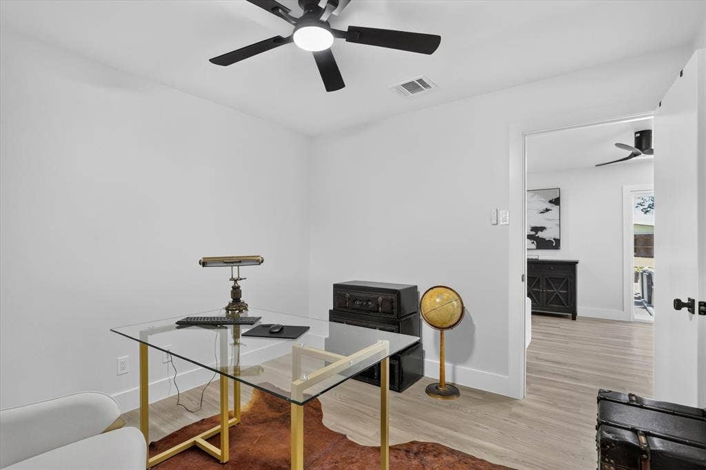 Neutral-toned interior space featuring wood-finish flooring, a matte black multi-blade ceiling fan with integrated lighting, and smooth-finish white walls
