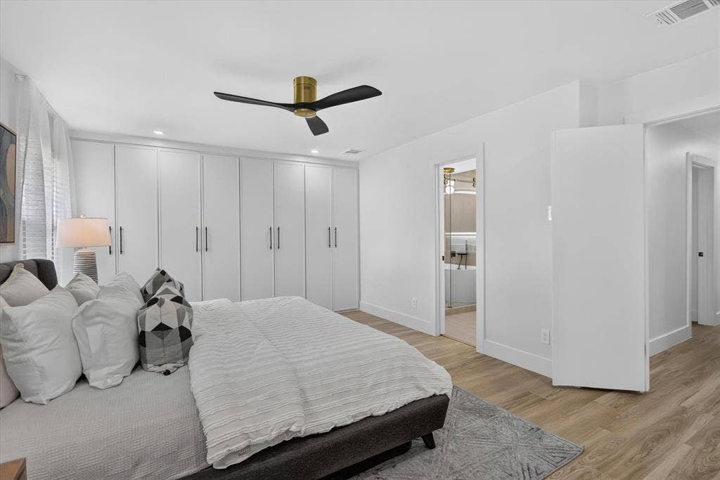 Full-wall custom white cabinetry, wood-finish flooring, and a modern ceiling fan with a metallic finish
