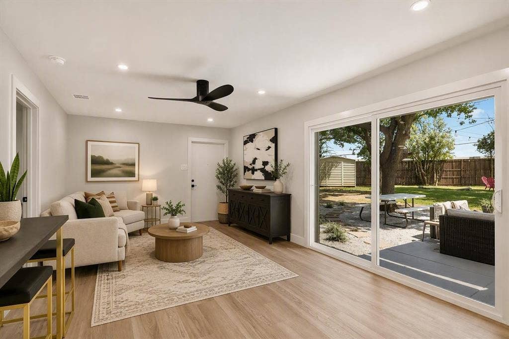 Living area featuring wood-finish flooring, recessed lighting, a modern ceiling fan, and large sliding glass doors opening to a stone-paved patio