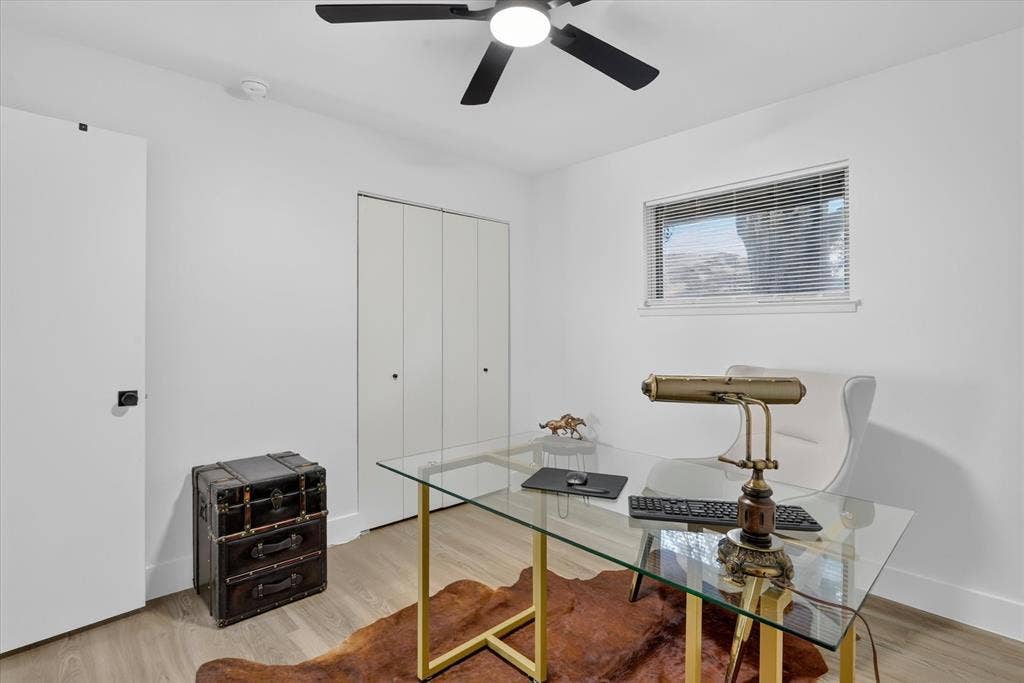 Neutral-toned room featuring wood-finish flooring, a multi-blade ceiling fan with integrated lighting, bifold closet doors, and a window with horizontal blinds