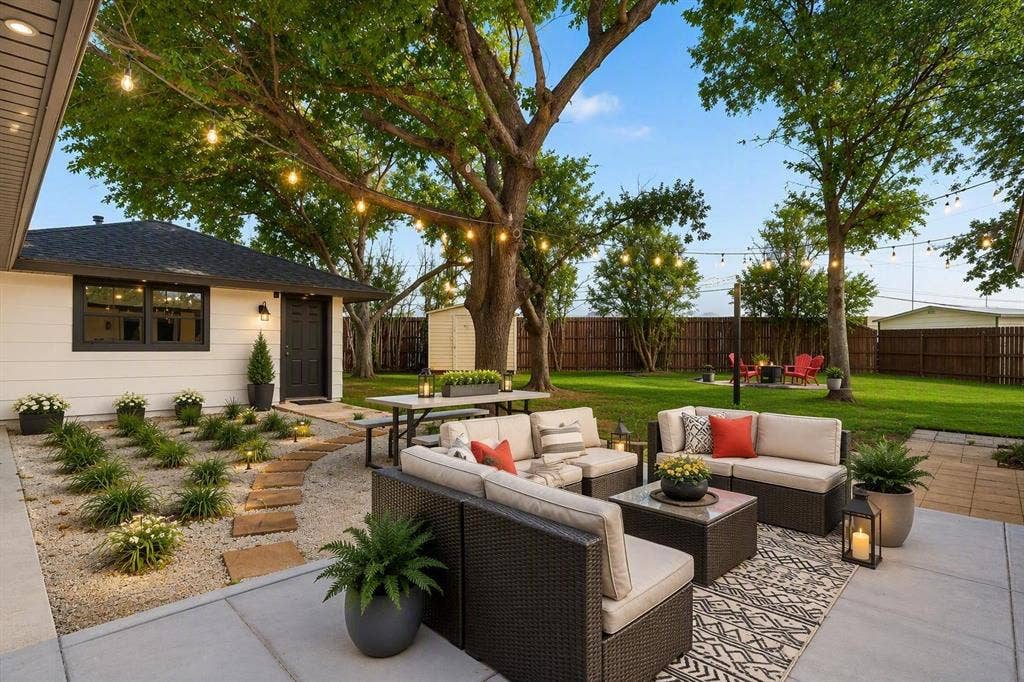 Backyard featuring concrete patio, gravel landscaping with stone paver path, mature trees, and wooden privacy fencing