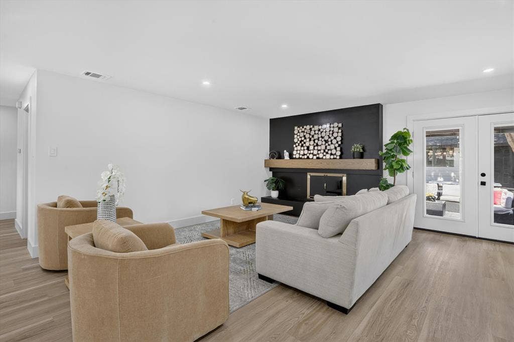 Living area featuring wood-finish flooring, a floor-to-ceiling black fireplace surround, a thick wood-beam mantel, and dual-pane glass patio doors