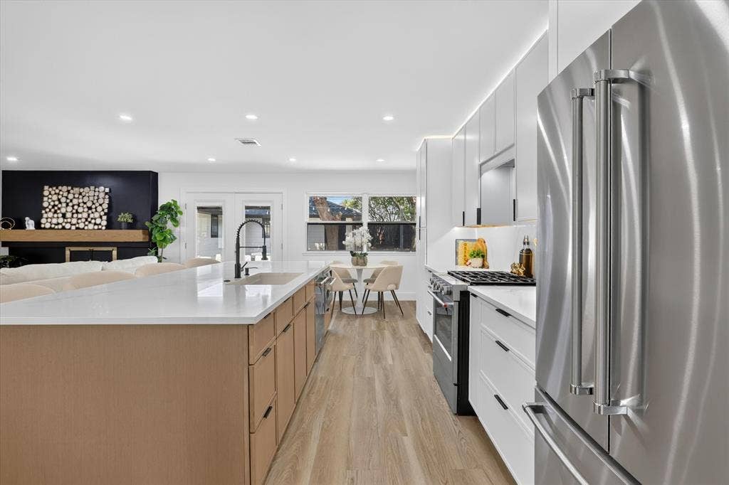 Kitchen featuring a large island with a quartz countertop, stainless steel appliances, flat-panel cabinetry, and wood-finish flooring