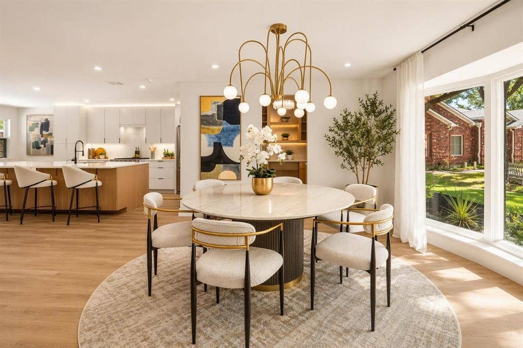 Open-concept interior featuring light wood-finish flooring, a contemporary multi-arm brass chandelier, built-in shelving with integrated lighting, and a large picture window