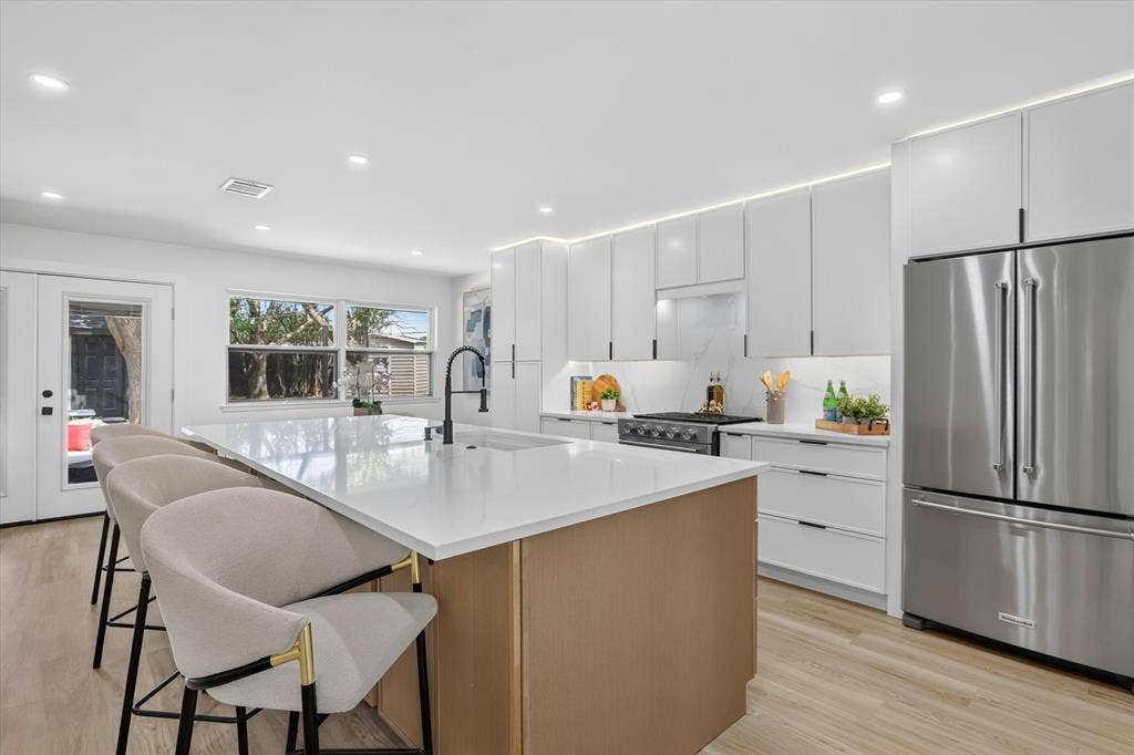 Kitchen featuring white cabinetry, wood-finish island, solid-surface countertops, stainless steel refrigerator, and recessed lighting