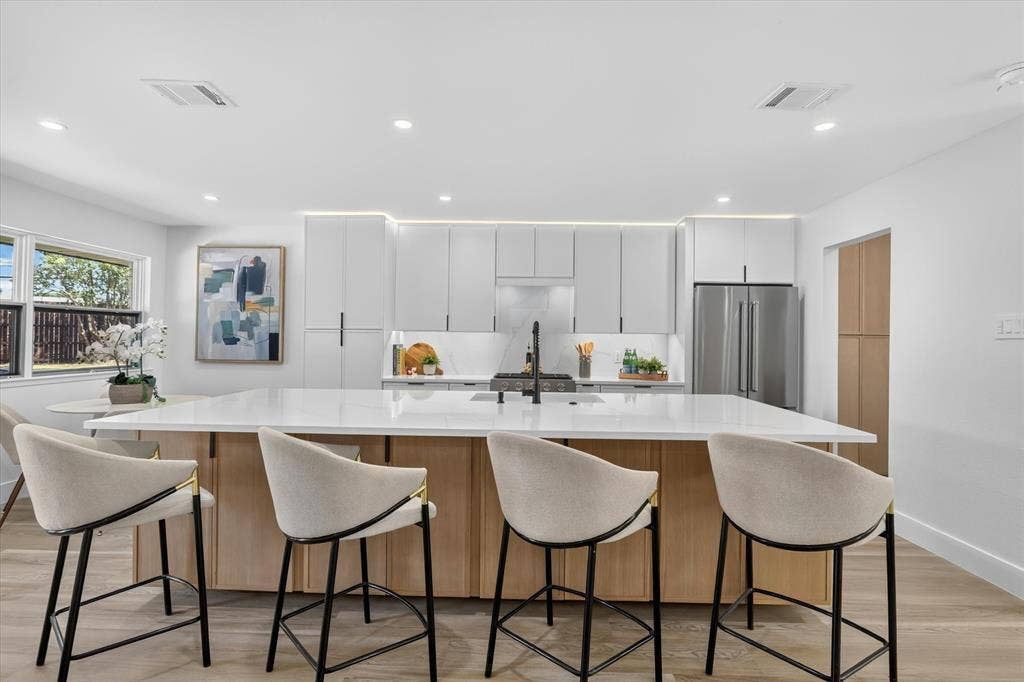 Kitchen featuring a large center island with a stone countertop, flat-panel white cabinetry, stainless steel refrigerator, recessed lighting, and wood-finish flooring