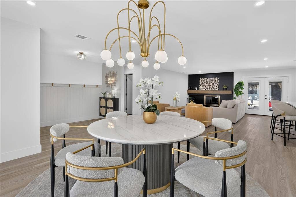 Open-concept area featuring wood-finish flooring, recessed lighting, a modern multi-arm chandelier with spherical globes, a black accent fireplace wall with a horizontal wood mantel, and wainscoting with integrated hooks