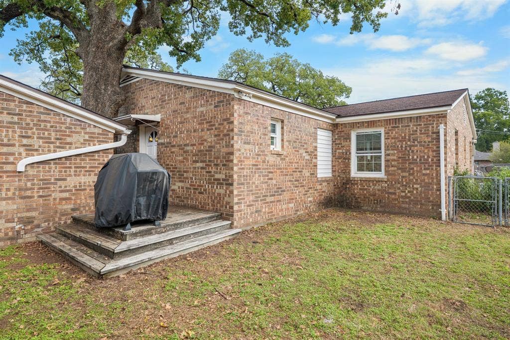 920 Avenue C, Lacy Lakeview, TX 76705 Exterior featuring a brick facade, multi-level wood deck, mature trees, and chain-link fencing
