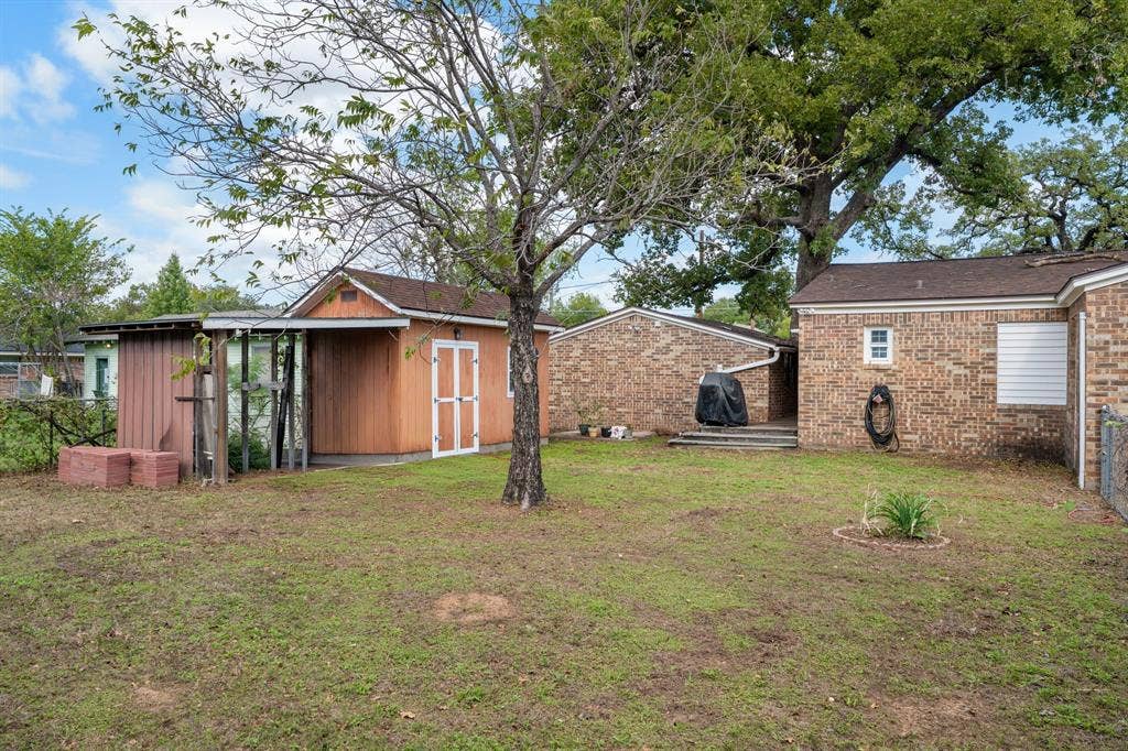 920 Avenue C, Lacy Lakeview, TX 76705 Backyard area featuring a brick-exterior residence, detached storage shed with double-entry doors, mature trees, and chain-link perimeter fencing