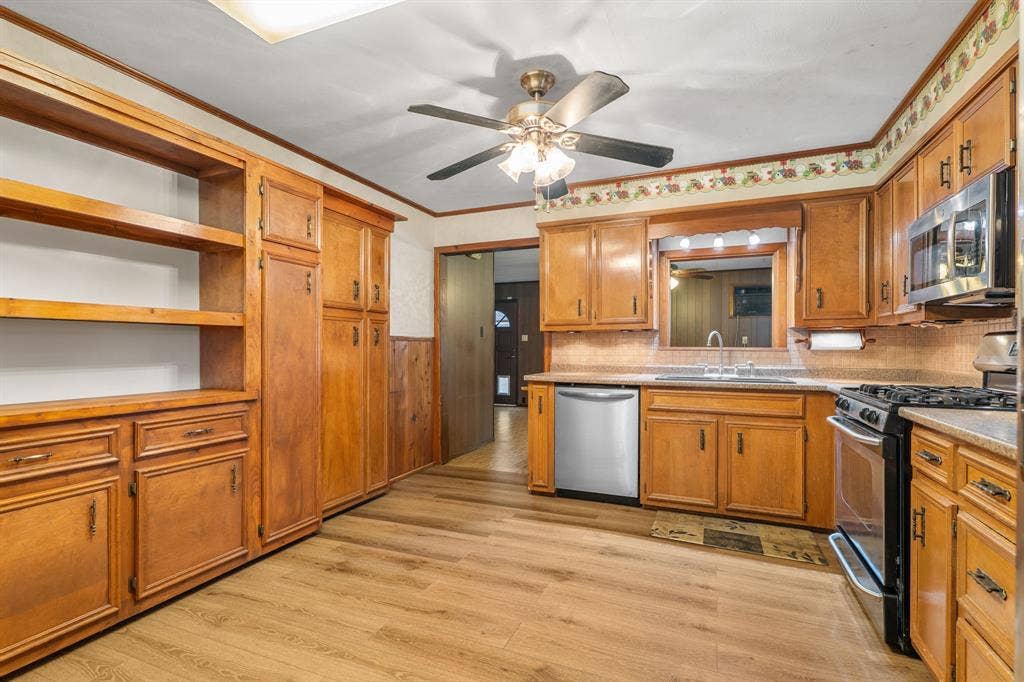 920 Avenue C, Lacy Lakeview, TX 76705 Kitchen featuring wood-finish cabinetry, built-in storage shelving, stainless steel appliances, wood-finish flooring, and a ceiling-mounted light fixture with a fan