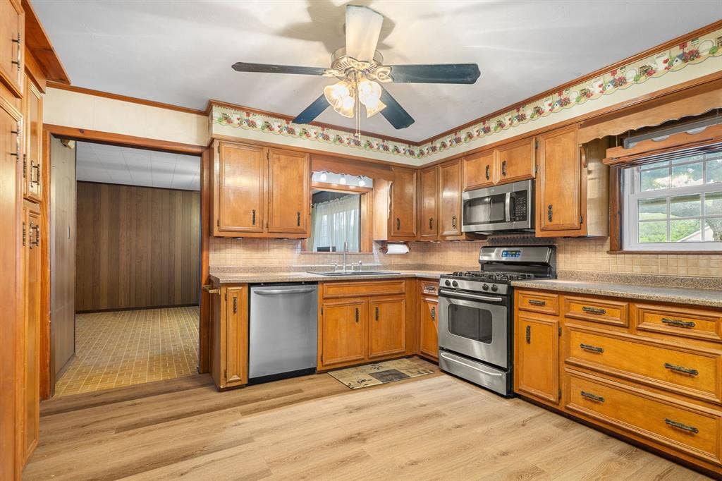 920 Avenue C, Lacy Lakeview, TX 76705 Kitchen featuring wood cabinetry, stainless steel appliances, wood-finish flooring, tiled backsplash, and a ceiling fan