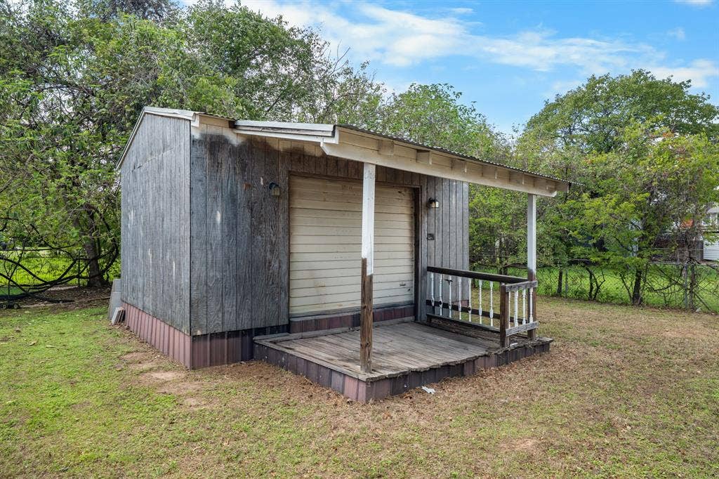 920 Avenue C, Lacy Lakeview, TX 76705 Detached storage structure featuring a metal-paneled roll-up door, covered front porch with a wooden deck, and a metal roof