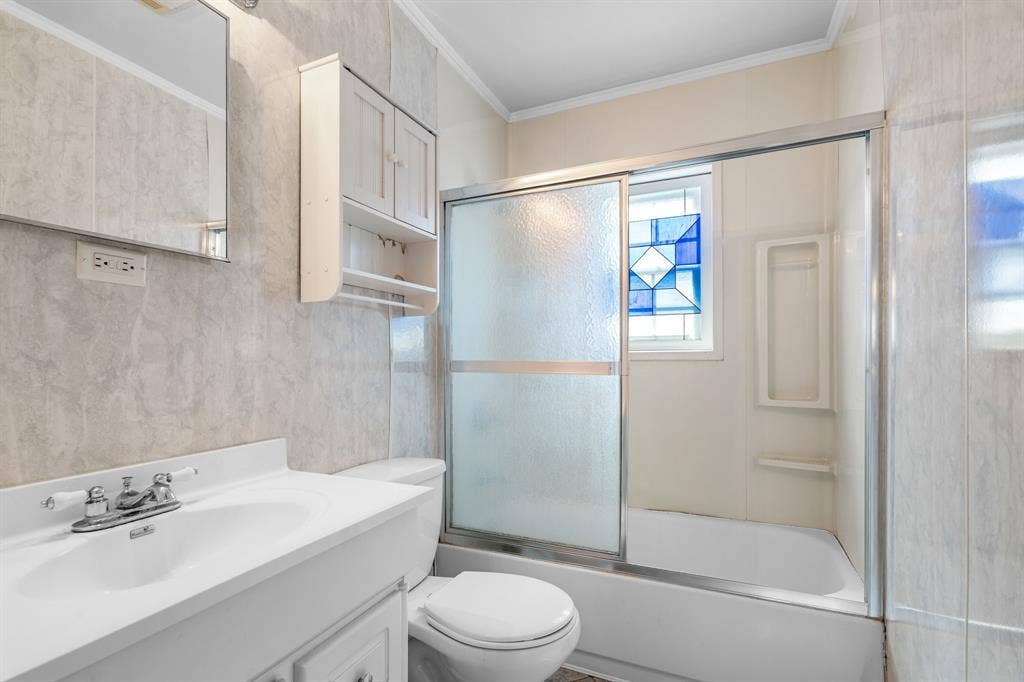 920 Avenue C, Lacy Lakeview, TX 76705 Bathroom featuring a vanity with an integrated sink, wall-mounted storage cabinet, sliding glass shower doors, tub surround with built-in shelving, and a decorative stained glass window
