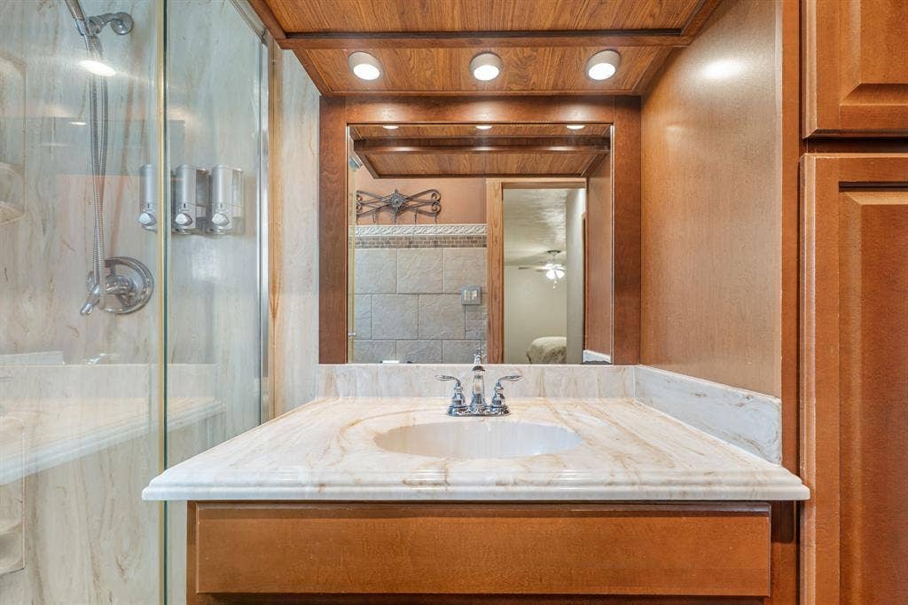 920 Avenue C, Lacy Lakeview, TX 76705 Custom wood-finish vanity with a stone countertop, integrated undermount sink, three-light recessed fixture, and glass-enclosed shower stall