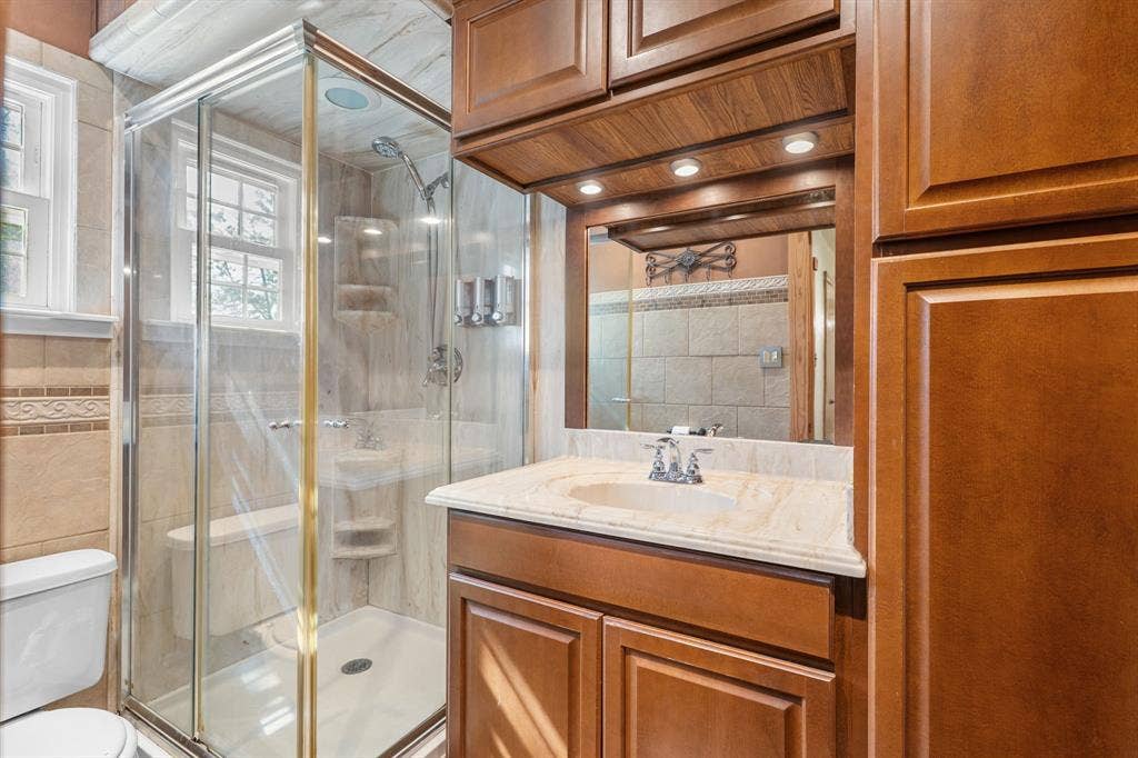 920 Avenue C, Lacy Lakeview, TX 76705 Bathroom featuring wood-finish cabinetry, stone-surface vanity countertop, glass-enclosed shower stall with integrated shelving, and recessed lighting