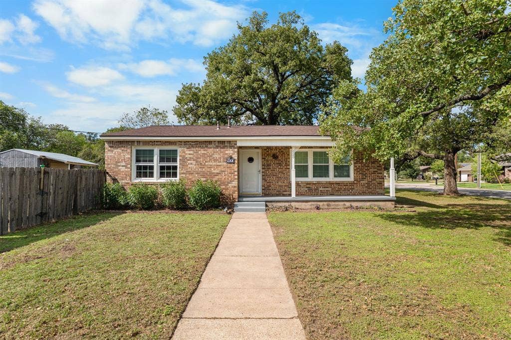 920 Avenue C, Lacy Lakeview, TX 76705 Brick exterior featuring a covered front porch, low-maintenance landscaping, and mature shade trees