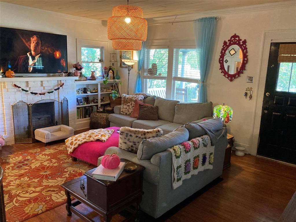 White-painted brick fireplace, built-in shelving, hardwood flooring, and a textured woven-shade pendant light