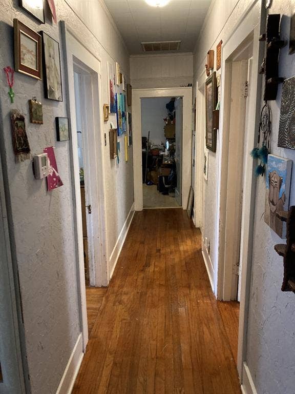 Hallway featuring wood-finish flooring, textured wall surfaces, and classic door casings