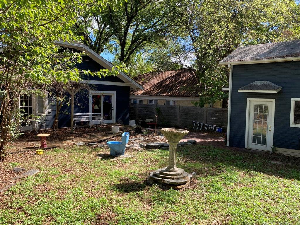 Exterior featuring dark lap siding, mature trees, a stone birdbath, and wood fencing